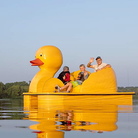 A family riding on the lake in a large yellow duck paddle boat.
