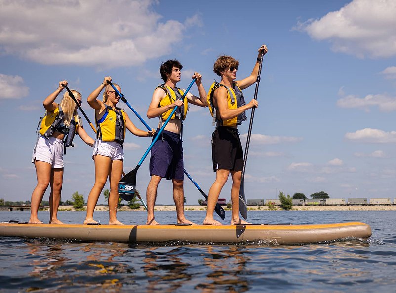 A group of four kids rowing together on a stand up paddle board.