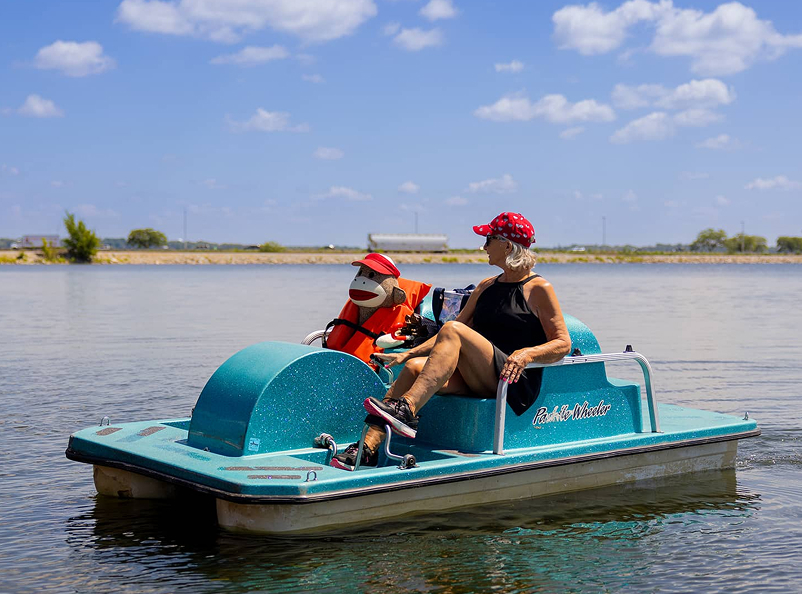 A woman on a paddle boat with her stuffed monkey. The monkey has a life vest.